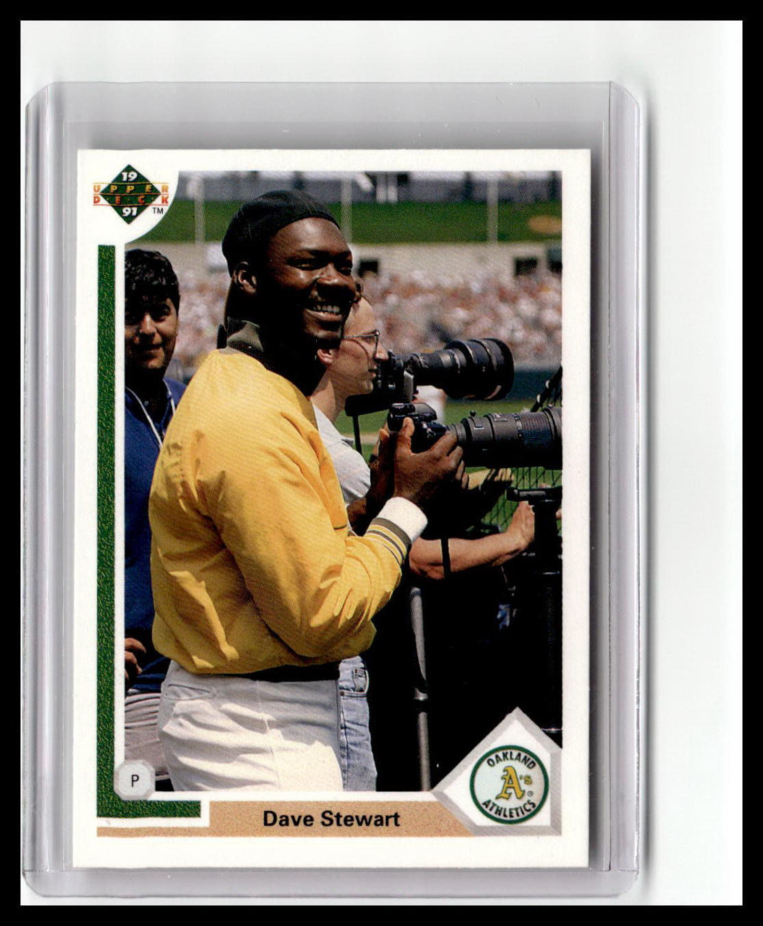 Baseball trading card of Dave Stewart holding a camera, with a sports field background.